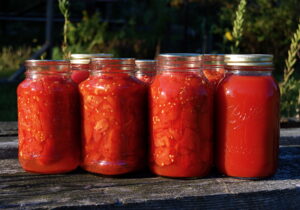 Tall jars full of bright red tomatoes sitting on an outside table.