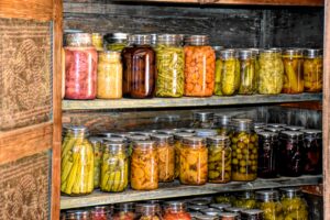 Jars of variously colored canned goods in a wooden cubbard.