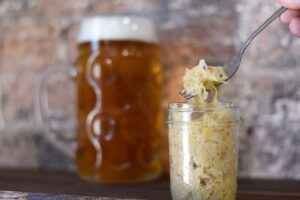 Sauerkraut being spooned from a jar in front of a large stein of beer.
