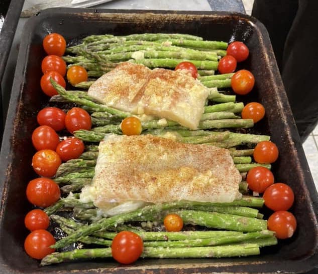Cod in a pan over asparagus and tomatoes.