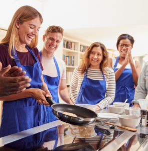 people smiling and wearing blue aprons, cooking on a stove with a pan